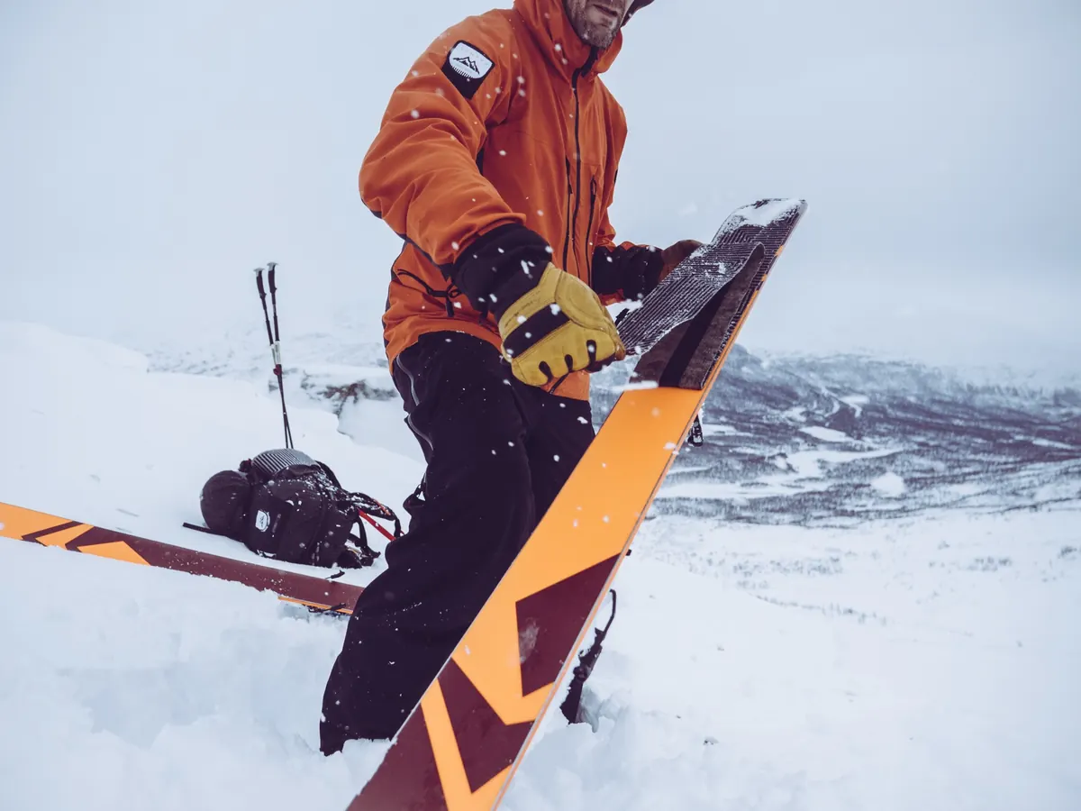 A guide in an orange jacket pulling the skins off the skis at a transition